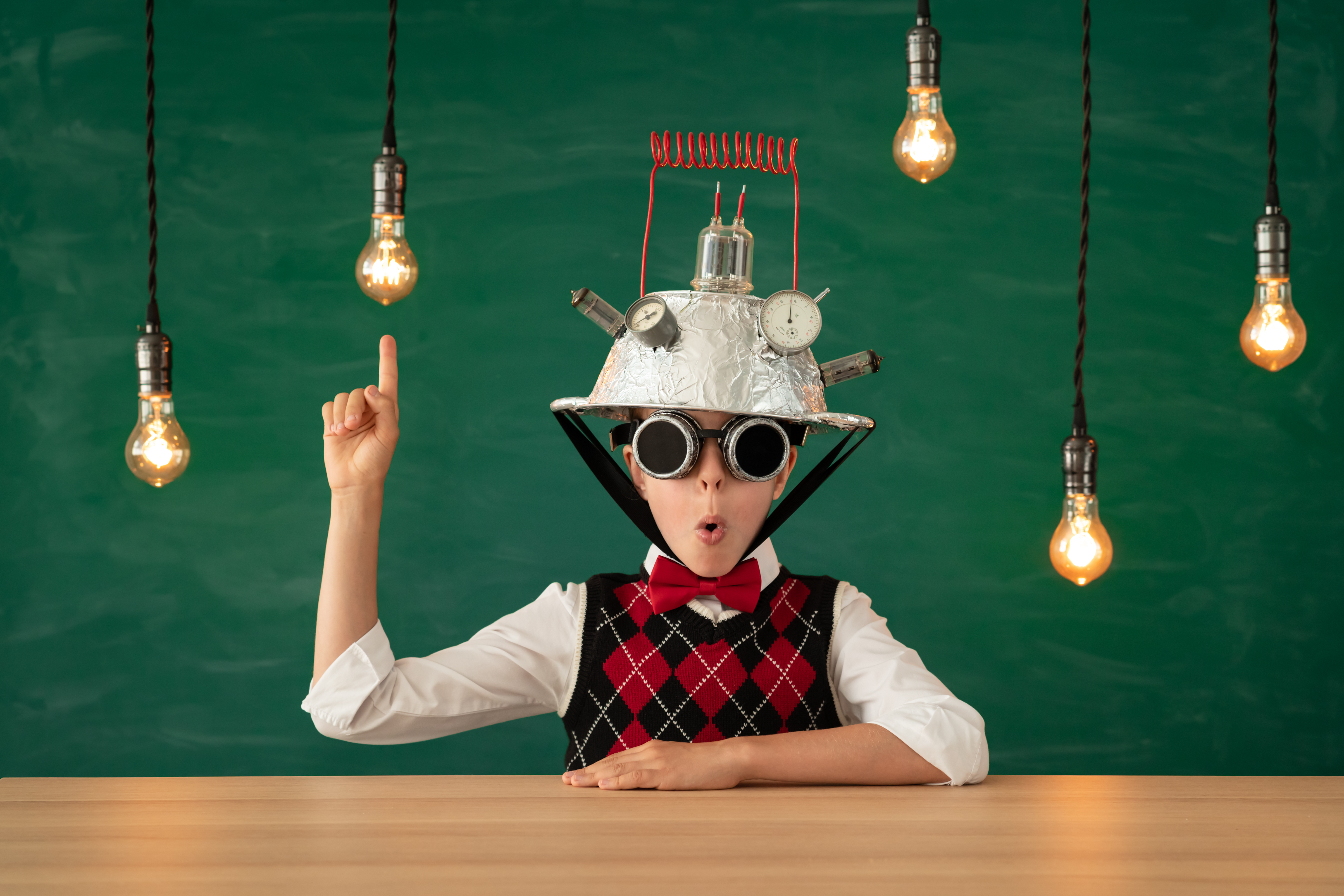 A happy student wearing a vest, bow tie, and an upside-down colander on his head, holding a finger up in the air as lightbulbs glow around him